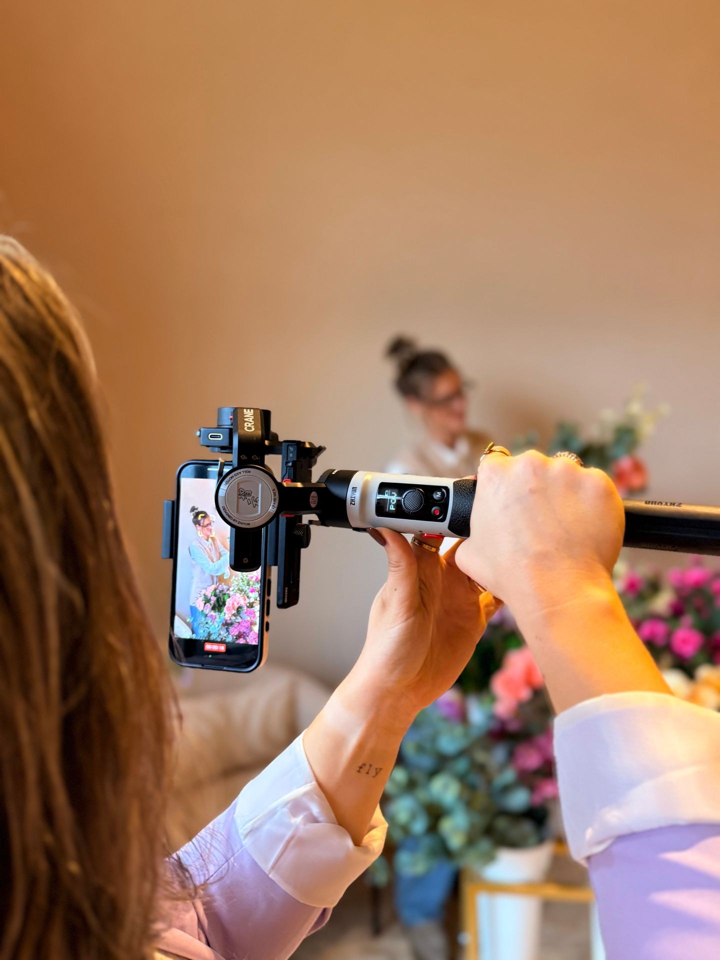 Person recording video with smartphone on gimbal in a flower shop setting.
